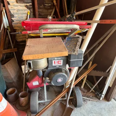 Red chipper shredder powered by an 8 HP Briggs & Stratton I/C engine, surrounded by various yard tools and equipment in a garage...