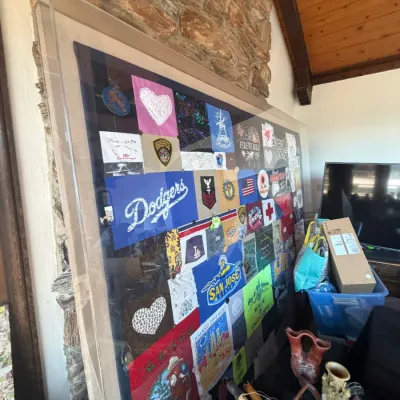 Large shadowbox acrylic display frame filled with a patchwork quilt of vintage t-shirt graphics, patches, and fabric swatches.