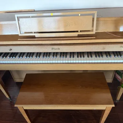 Mid-century modern light wood Starck spinet piano with matching bench, featuring clean geometric lines and taper legs.