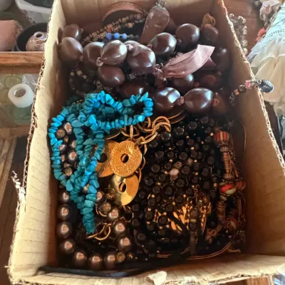 Cardboard box filled with assorted vintage costume jewelry, including seed nut necklaces, faux turquoise chip strands, metallic beads,...