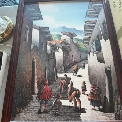 Framed Peruvian oil painting depicting a village street scene with figures and llamas in traditional Andean attire.