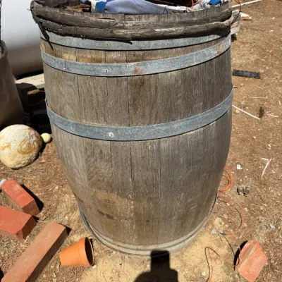 Rustic weathered oak wooden barrel with metal hoops, filled with various miscellaneous yard debris and items.