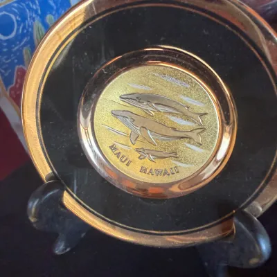 Vintage Maui, Hawaii souvenir decorative mini plate featuring relief humpback whales and a metallic gold-tone rim, displayed on a small...