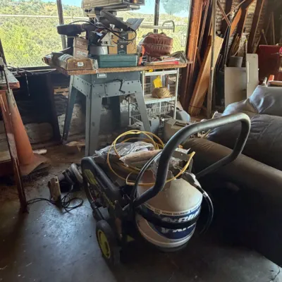 Sun Joe wheeled pressure washer with propane tank attached, alongside a vintage radial arm saw mounted on a metal stand.