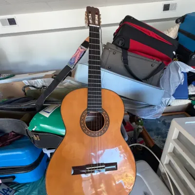 Classical acoustic guitar featuring a natural finish top, decorative rosette around the soundhole, slotted headstock, and an attached...