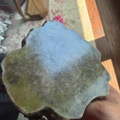 Polished green marble or onyx top section of a small carved pedestal, showing visible surface scuffs and wear from use.