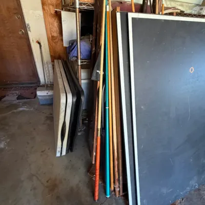 Assorted billiard cues, a folding ping pong table top, and folding plastic utility tables stored in a garage.