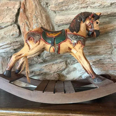 Hand-carved and painted vintage wooden rocking horse with decorative saddle details, metal stirrup, and natural hair tail.