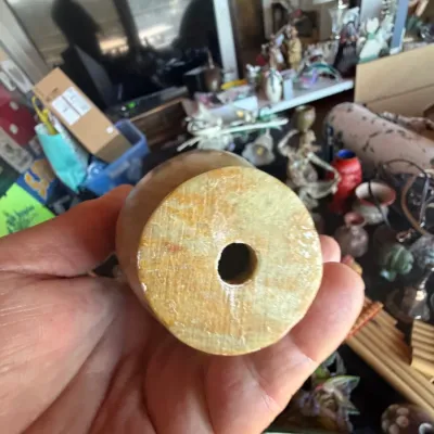 Handheld view showing the bottom base with a central hole of a carved stone or alabaster vessel.
