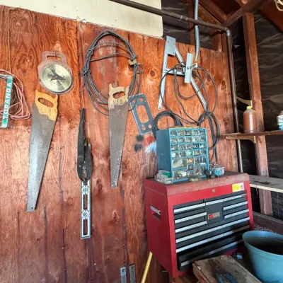 Workshop wall featuring mounted hand saws, level, and circular saw blade, paired with a red multi-drawer metal toolbox and blue parts...