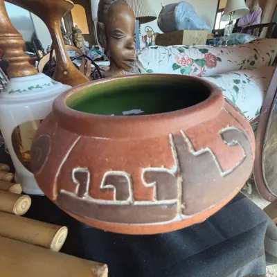 Terracotta ceramic bowl with carved geometric details and a green glazed interior, displayed alongside carved wood decor and home...
