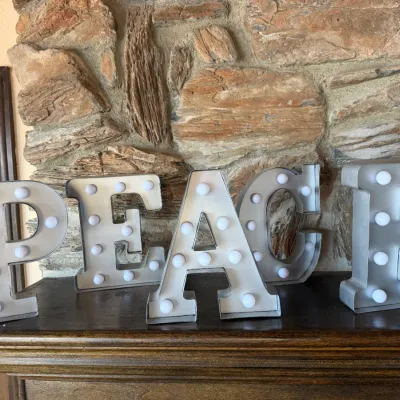 Metal marquee letter sign spelling 'PEACE' with white bulb lights, displayed on a wooden fireplace mantel.