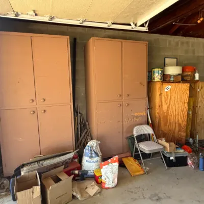 Two tall, dusty peach painted garage storage cabinets flanked by plywood utility cabinets, folding chair, and miscellaneous lawn and...