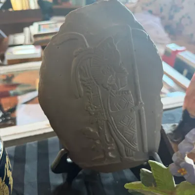 Hand-carved stone slab featuring a Mayan or Aztec warrior figure, displayed on a black metal stand.