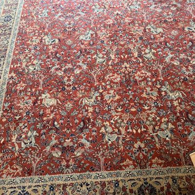 Sale Photo Thumbnail #150: Large Persian-style area rug featuring a dense pictorial hunting pattern with figures on horseback, animals, and flora on a red field.