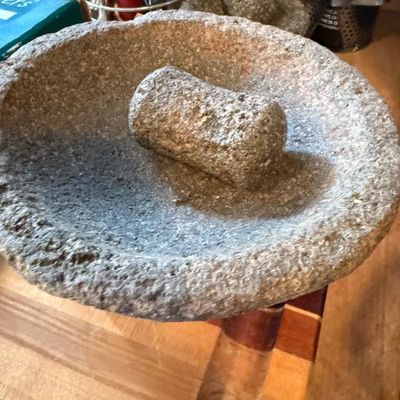 Sale Photo Thumbnail #367: Rustic carved granite mortar and pestle set resting on a wooden surface.