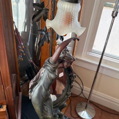 Sale Photo Thumbnail #251: Art Nouveau style figural metal table lamp featuring a draped female maiden reaching toward a ruffled frosted glass shade with leaf accents.
