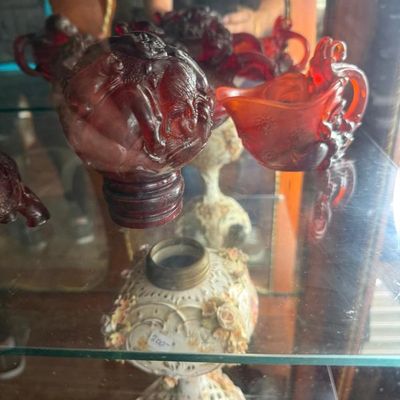 Sale Photo Thumbnail #281: Collection of decorative glassware displayed in a cabinet, including a carved red slag glass globe feature and ornate porcelain lamp bases with floral accents.