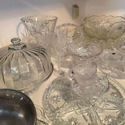 Sale Photo Thumbnail #309: Collection of clear cut glass and pressed glass serveware, including a ribbed cake dome, punch bowl, starburst platter, champagne flutes, and a stainless steel saucepan.