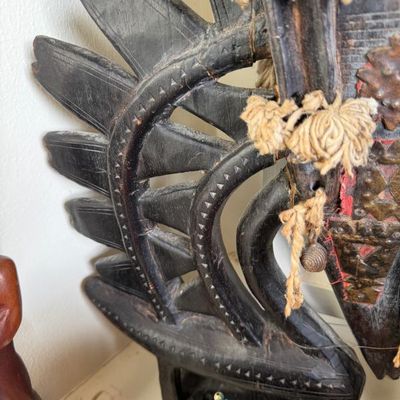 Sale Photo Thumbnail #220: Detail of an ornate African wooden headdress sculpture, featuring hand-carved openwork, geometric patterns, and fiber tassels.