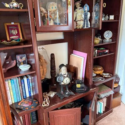 Sale Photo Thumbnail #244: Large dark wood hutch and wall unit filled with collectibles, including vintage dolls, decorative clocks, books, and figurines.