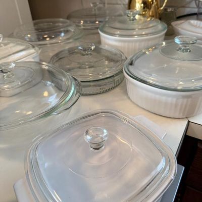 Sale Photo Thumbnail #373: Collection of vintage CorningWare and Pyrex baking dishes with clear glass lids, displayed alongside a gold-tone thermal carafe.
