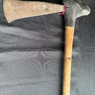 Sale Photo Thumbnail #203: African tribal style axe featuring a flared iron blade with etched details set into a hand-carved wooden handle with textured geometric patterns.