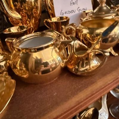 Sale Photo Thumbnail #349: Collection of vintage Hall China 'Golden Glow' gold-plated teapot, sugar bowl, and cream pitchers displayed on a wooden shelf.