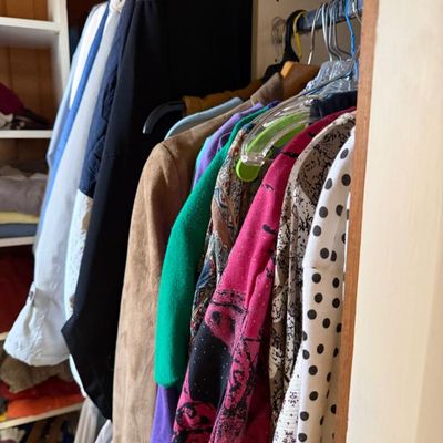 Sale Photo Thumbnail #240: Assorted vintage and modern women's clothing, including jackets, blouses, and patterned tops hanging inside a closet.