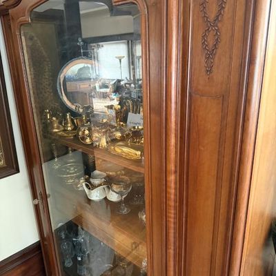 Sale Photo Thumbnail #151: French Provincial style carved wood display cabinet with glass door and interior shelves, housing various gold-tone and crystal glassware items.