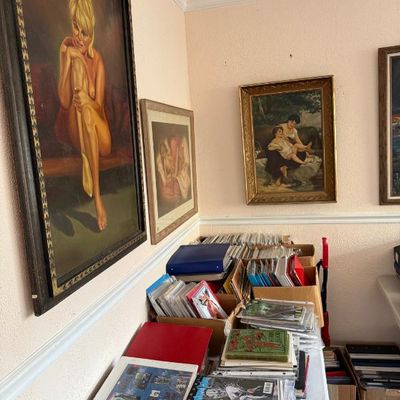 Sale Photo Thumbnail #191: Mid-century vintage blonde pin-up portrait framed artwork hanging above tables stacked with books, binders, and collectibles.
