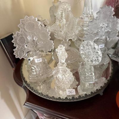 Sale Photo Thumbnail #275: Collection of vintage cut glass vanity perfume bottles displayed on a round mirror tray, featuring decorative floral stoppers.