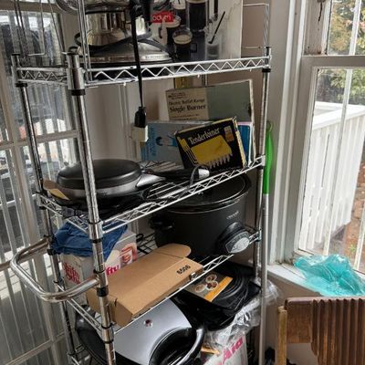 Sale Photo Thumbnail #374: Chrome wire baker's rack filled with various small kitchen appliances and accessories, including a slow cooker, electric urn, waffle maker, and boxed goods.