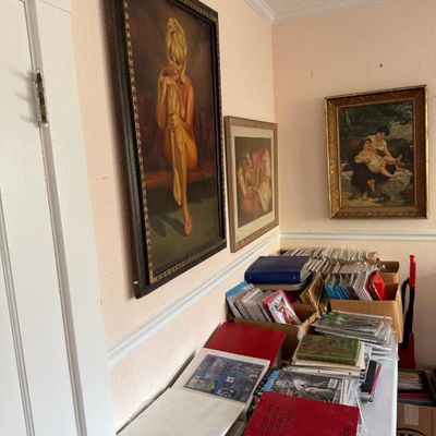 Sale Photo Thumbnail #194: Collection of vintage framed artwork hanging on a wall above folding tables packed with vinyl records, binders, and books.