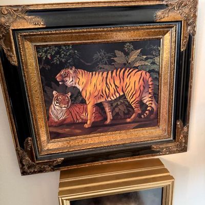 Sale Photo Thumbnail #106: Framed jungle scene painting featuring two tigers set in an ornate black and gold-toned decorative frame.