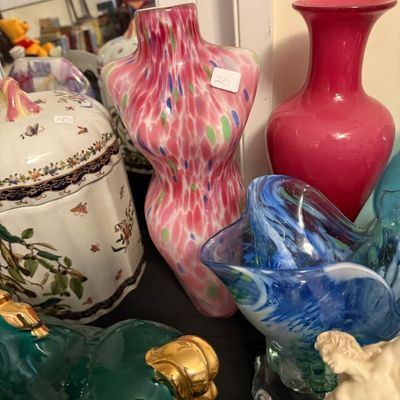 Sale Photo Thumbnail #160: Collection of decorative glass and ceramic items, including a pink splatter-pattern torso vase, a ruby red blown glass vase, and an ornate blue art glass bowl.