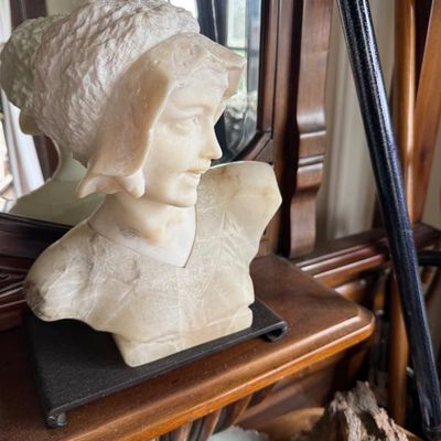 Sale Photo Thumbnail #293: Antique carved alabaster marble bust of a young woman wearing a bonnet, mounted on a dark pedestal base.