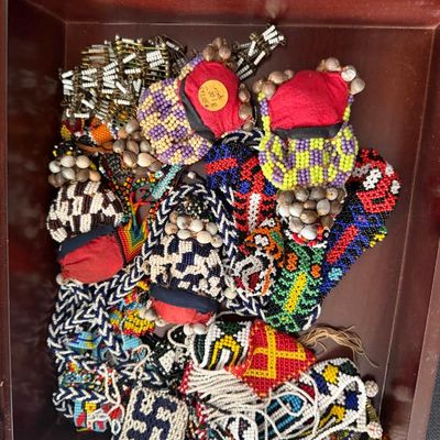 Sale Photo Thumbnail #215: Collection of vintage beaded African pouches and tribal jewelry featuring intricate multi-colored seed bead patterns and natural accent beads, displayed in a wooden tray.