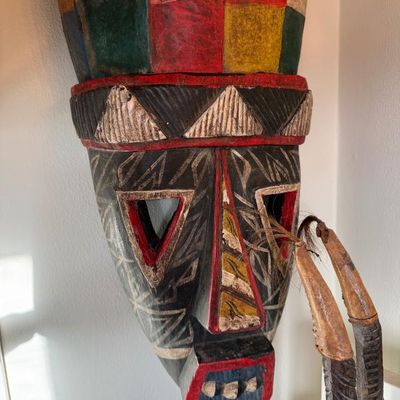 Sale Photo Thumbnail #221: Hand-carved and painted African-style wooden tribal mask featuring geometric patterns, triangular eye cutouts, and a colorful crown.