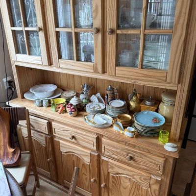 Sale Photo Thumbnail #314: Rustic pine hutch and buffet featuring glass-front cabinet doors, multiple drawers, and display shelves filled with decorative tableware and collectibles.