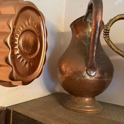 Sale Photo Thumbnail #300: Vintage copper kitchenware, including an oval gelatin mold hanging on the wall and a small footed copper pitcher with verdigris patina.