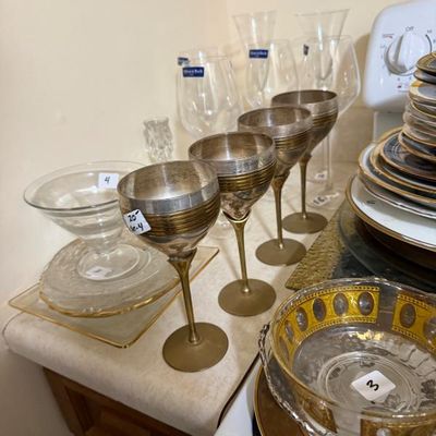 Sale Photo Thumbnail #169: Set of four silverplate and brass stemmed goblets shown alongside clear glassware and gold-rimmed serveware on a kitchen counter.