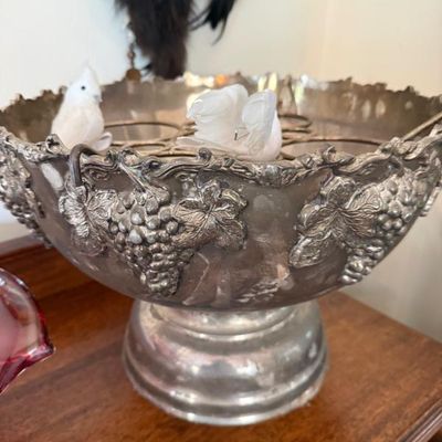 Sale Photo Thumbnail #14: Vintage silver-plated punch bowl featuring embossed grape and vine motifs around the rim, set on a pedestal base with decorative white bird figures inside.