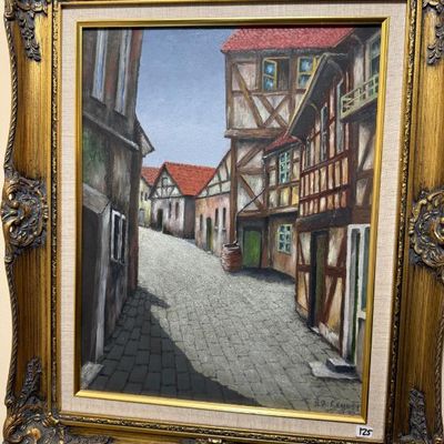 Sale Photo Thumbnail #51: Framed oil painting depicting a European village street lined with half-timbered buildings, set in an ornate gilded frame with a linen liner.