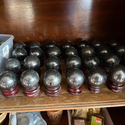 Sale Photo Thumbnail #261: Collection of polished metallic stone spheres arranged on dark carved wooden stands on a shelf.