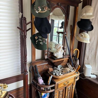 Sale Photo Thumbnail #298: Antique wooden hall tree with mirror, lower storage cabinet, umbrella stands, and displayed hats including Tyrolean styles with pins.