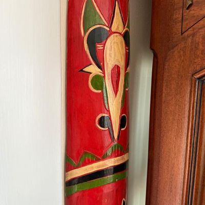 Sale Photo Thumbnail #231: Hand-painted wooden mask or wall hanging featuring a vibrant red background with stylized green, yellow, and black carved accents.
