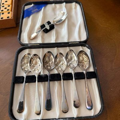 Sale Photo Thumbnail #6: Set of seven vintage silver-plated fruit demitasse spoons with embossed fruit bowls, displayed in their original satin-lined presentation box with some visible tarnish.