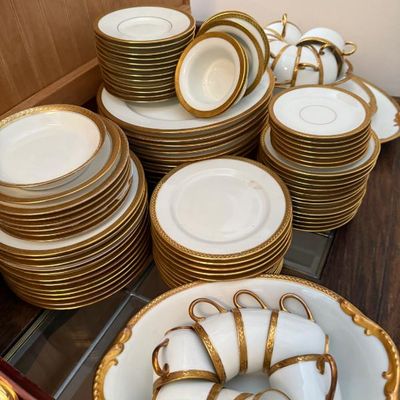Sale Photo Thumbnail #9: Extensive fine porcelain china dinnerware set featuring white porcelain trimmed with heavy gold filigree rims, including stacks of plates, saucers, small bowls, and teacups.