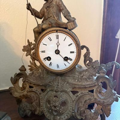 Sale Photo Thumbnail #359: Antique French figural mantel clock featuring a metal sculpture of a young boy fisherman seated atop an ornate, acanthus-scroll base.